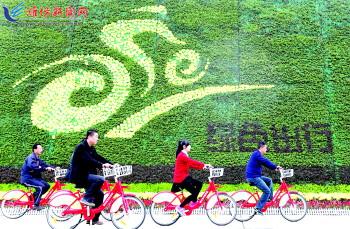市民騎公共自行車路過市人民廣場一處花壇。記者 張馳